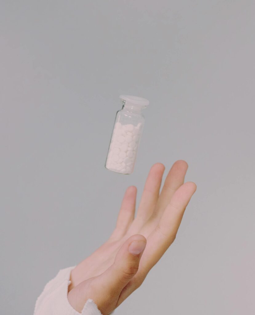 Hand in focus tossing a pill vial against a subtle gray backdrop.